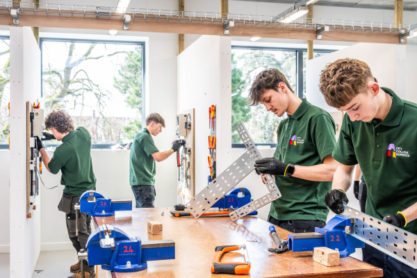 Two electrical students working at a work bench in the foreground and a pair of students working in a bay in the background.